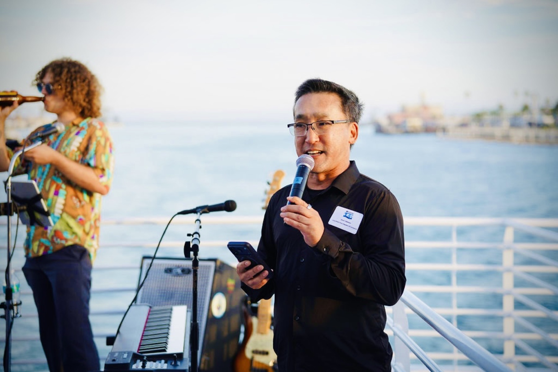 Stuart Takehara speaks into a microphone aboard Harbor Breeze with the Long Beach waterfront in the background